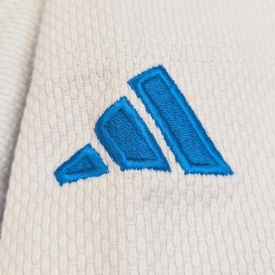 Szczegóły trzech pasków Adidas i niebieskiego logo w wersji włoskiej na ramieniu judogi