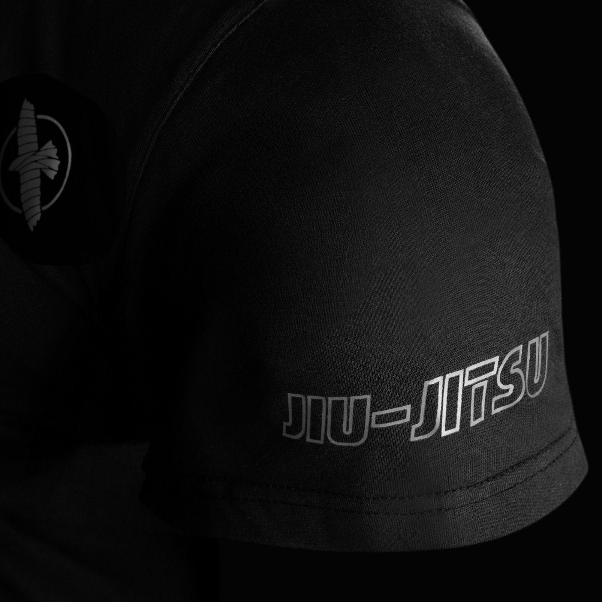 Close-up detail of the sleeve of the black Hayabusa UFC BJJ t-shirt, showing the reinforced stitching and the embroidered falcon logo